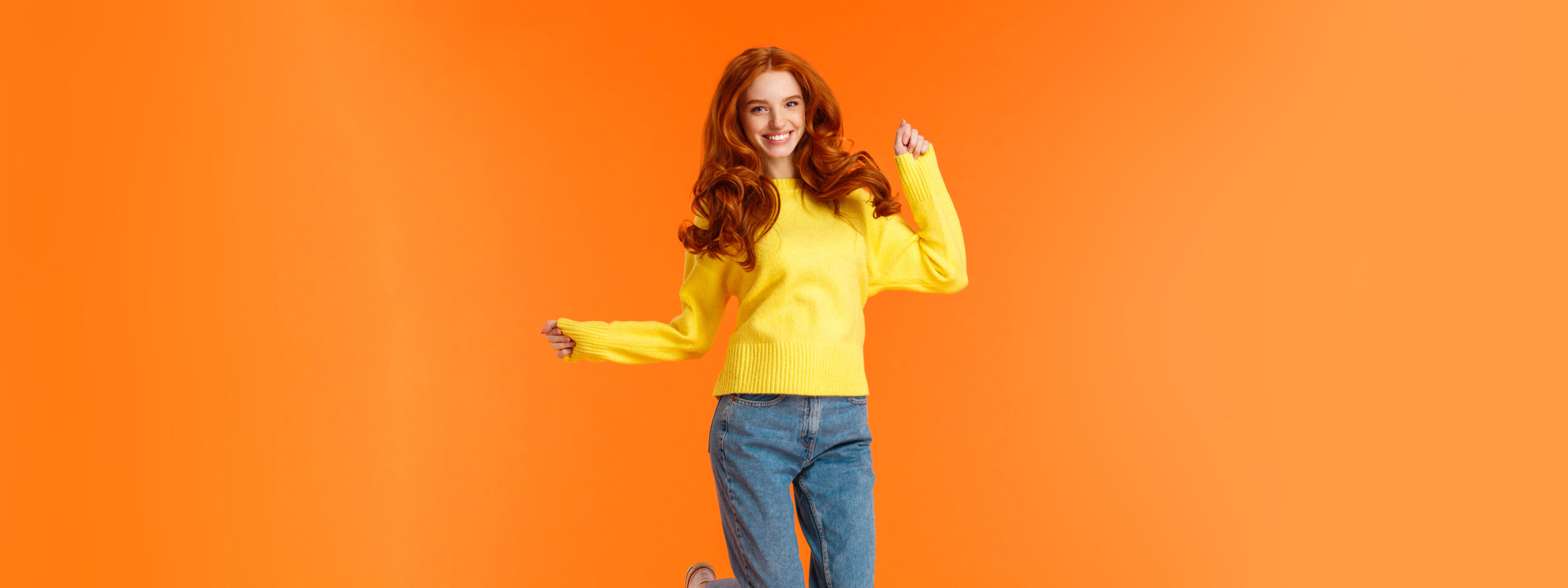 Vertical full-length portrait cheerful redhead excited girl jumping and feeling happy, smiling gazing camera carefree, cant wait open presents on winter holidays party, orange background.